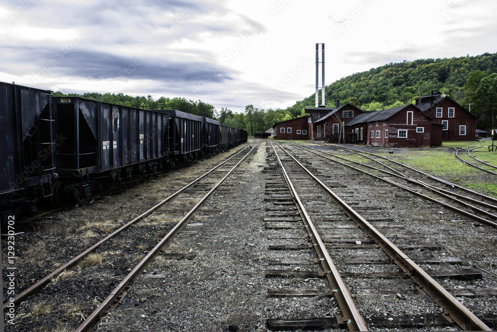 tracks running through old railroad yard next to rusting coal hoppers and maintenance shops