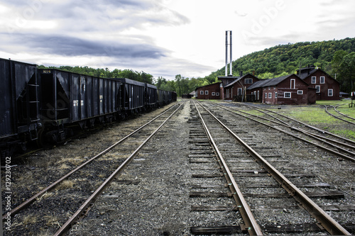 tracks running through old railroad yard next to rusting coal hoppers and maintenance shops