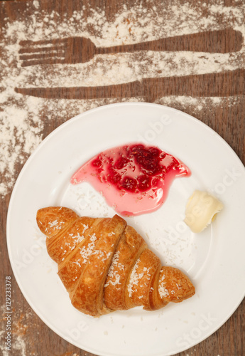It lies on a plate with croissants, jam and butter, sprinkled with powdered sugar
