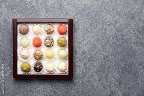 Various chocolate truffle candies in a box on gray stone background