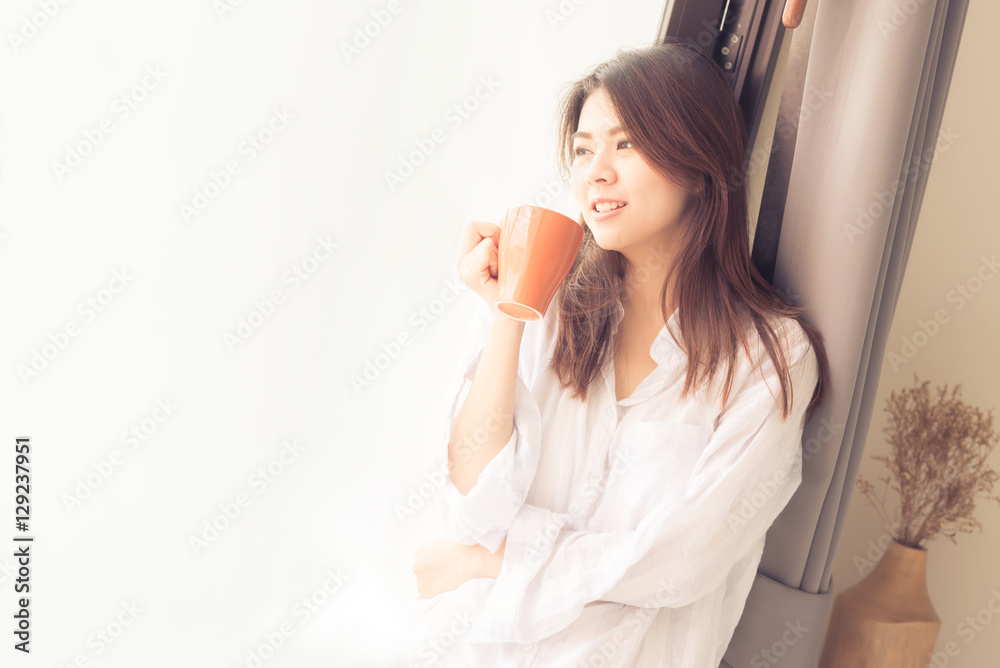 Happy beautiful young Asian woman smile while drinking coffee in morning by window Happy beautiful young Asian woman smile while drinking coffee in morning by window