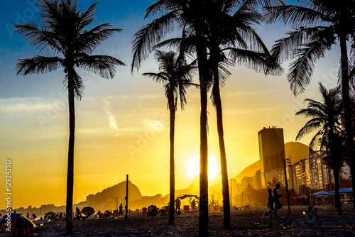 Beautiful bright sunset on Copacabana beach with palm trees and silhouettes of people walking at the beach  Rio de Janeiro  Brazil