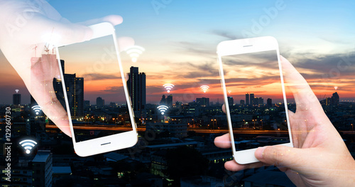 Internet of things , iot , smart home , smart city and network connect concept. Hands holding white phones and wifi icon with city sunset view.