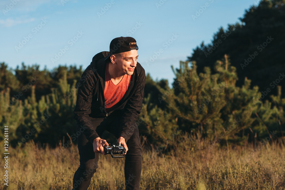 Pleased guy running drone outdoor, free space. Young smiling man recklessly piloting rc toy in meadow. Excited of new entertainment male adult. Leisure, fun, joy concept Pleased guy running drone outdoor, free space. Young smiling man recklessly piloting rc toy in meadow. Excited of new entertainment male adult. Leisure, fun, joy concept