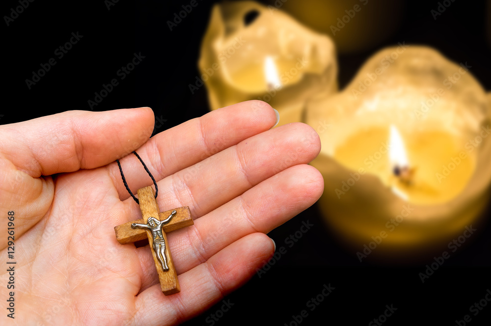 Fototapeta premium Female hand with wooden cross on candles background