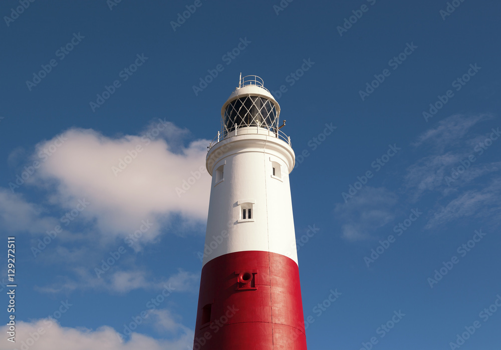 Close up of the lighthouse at Portland Bill completed in 1906 to keep shipping away from the nearby cliffs and rocks. Sunny day with clouds in the sky. Space for text.