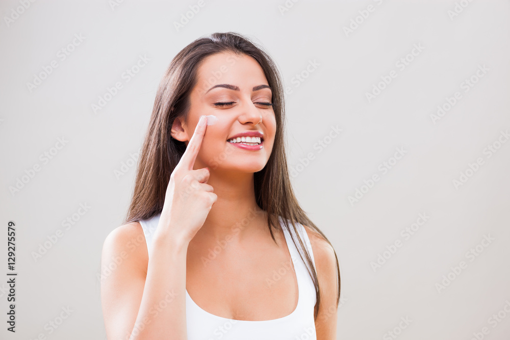 Portrait of young woman who is applying skin cream on her face. Portrait of young woman who is applying skin cream on her face.