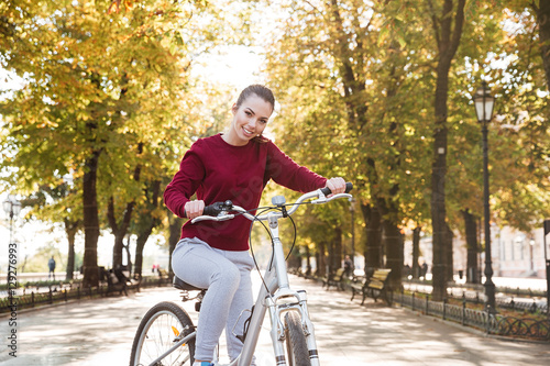 Happy lady dressed in sweater walking with her bicycle