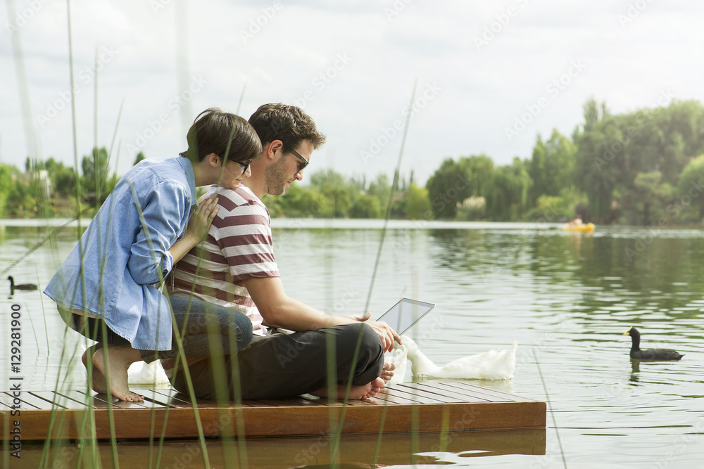 Couple using a laptop while sitting on dock Couple using a laptop while sitting on dock
