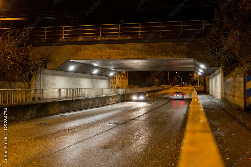 Gatubelysning under järnvägsbro med körandes bilar på kvällen