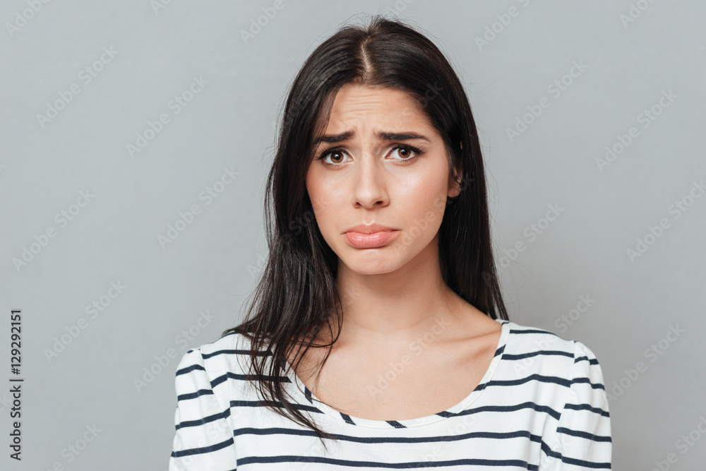 Sad young woman standing over grey background Sad young woman standing over grey background
