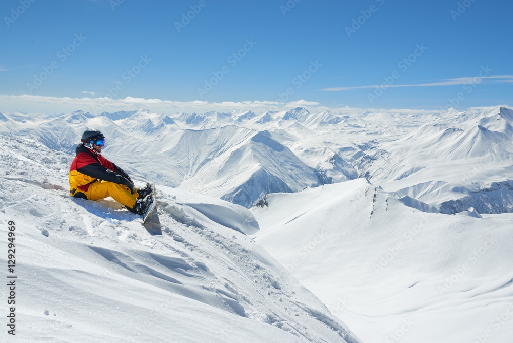 snowboarder sits high in mountains on the edge of slope