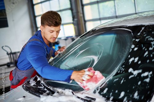 Man worker washing windshield with sponge on a car wash
