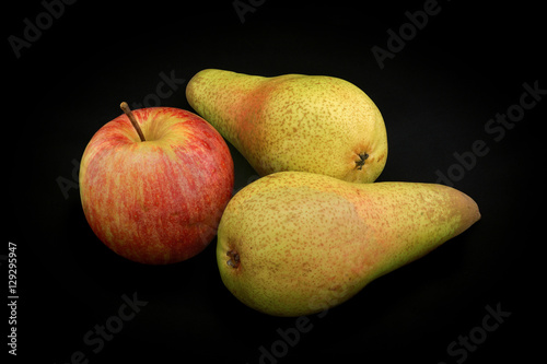 Apple of red color and two pears of yellow color on a black back
