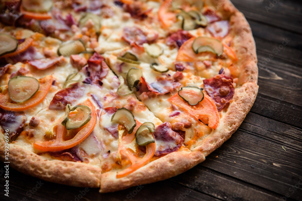 Pizza with salami, pickles, tomatoes, cheese and ham on a dark wooden background, top view