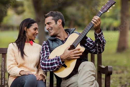 Smiling man with woman playing guitar on bench