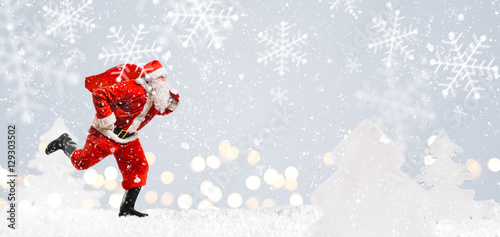 Santa Claus running at New Year or Christmas delivery rush with gift bag full of presents on snow