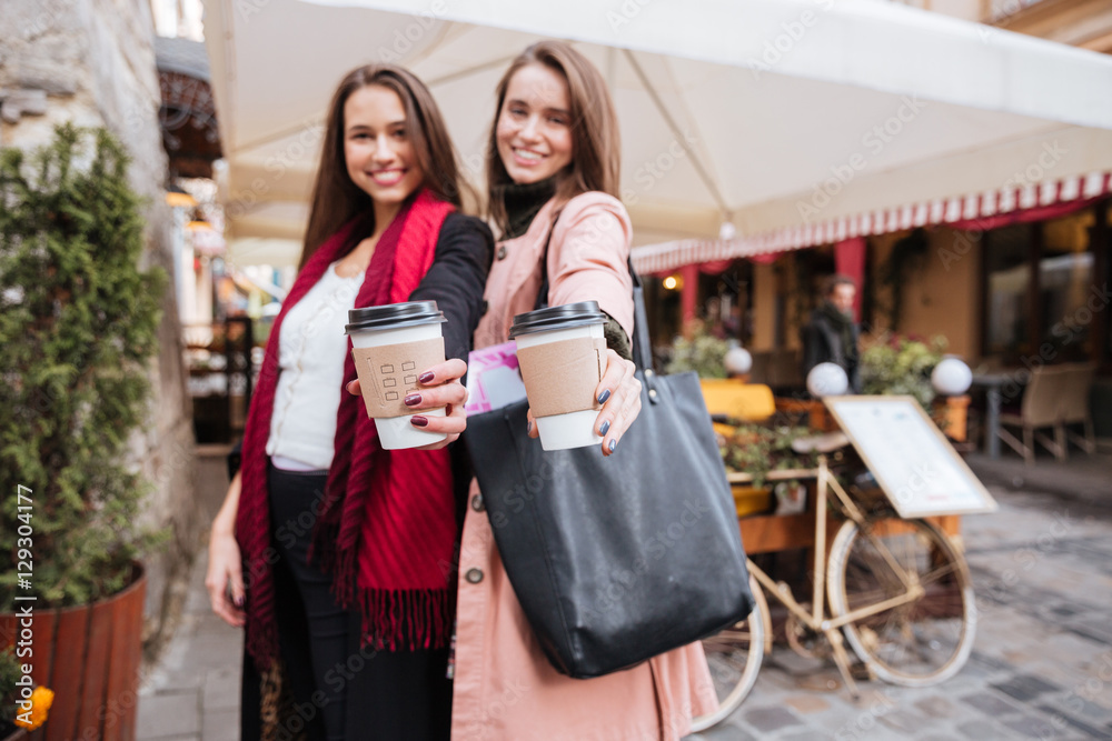 Two smiling attractive young women holding cups of takeaway coffee Two smiling attractive young women holding cups of takeaway coffee