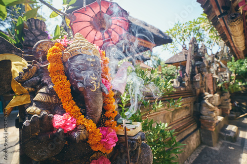 Religious decoration. Traditional stone sculpture of Ganesha god with flowers in the backyard. Bali, Indonesia.