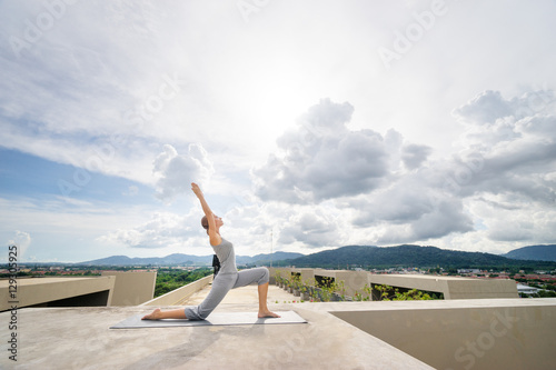 Yoga on rooftop. Happy young woman stretching on roof with city and mountains view.