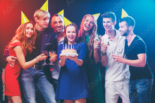Happy birthday! Group of smiling friends gathered together around young woman with cake.