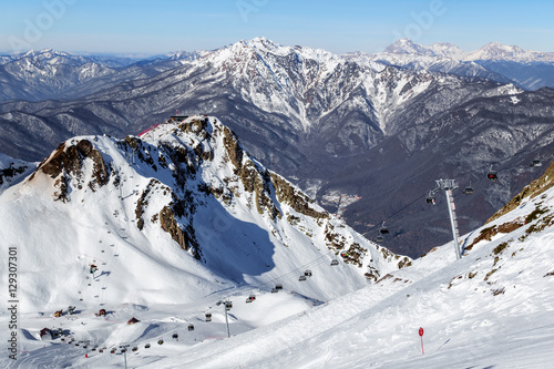 Ski slopes and chair ski lifts in Sochi winter mountain ski resort on blue sky and snowy peaks scenic background