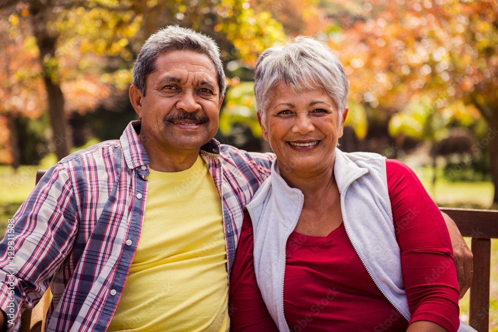 An elderly couple smiling at the camera sitting on the bench An elderly couple smiling at the camera sitting on the bench