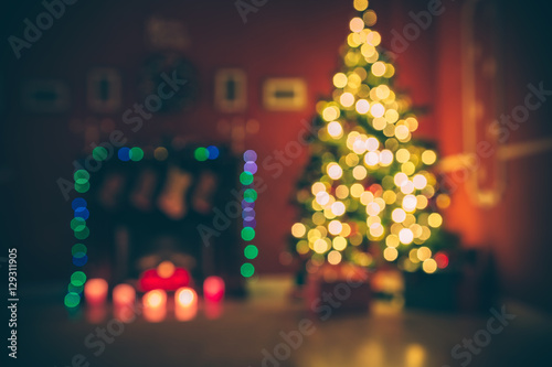 Fotografie, Obraz Beautiful  Defocused background new year room with decorated Christmas tree, gifts and fireplace with the glowing lights at night