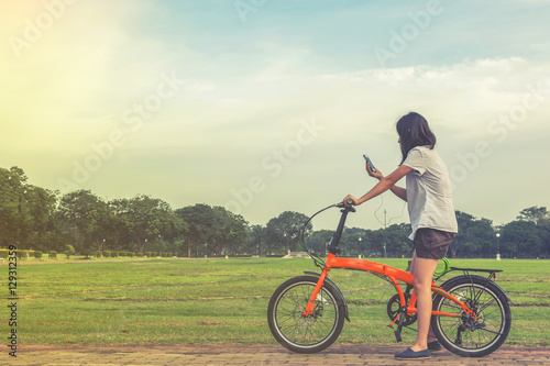 Fototapeta Naklejka Na Ścianę i Meble -  Pretty young woman using smartphone with riding bicycle in park