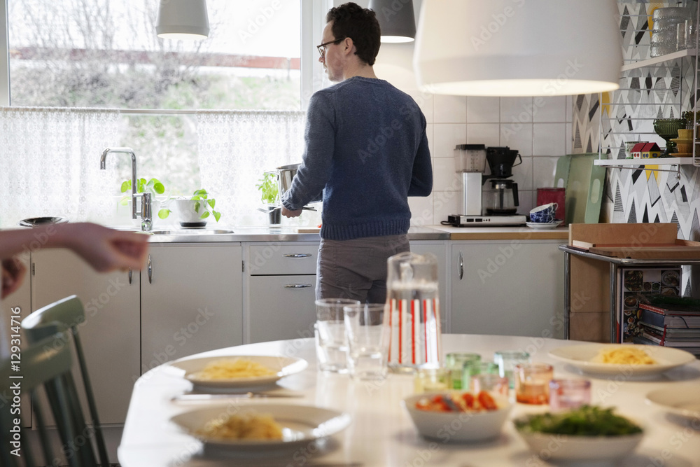 Food served on table against man standing by kitchen counter at home Food served on table against man standing by kitchen counter at home