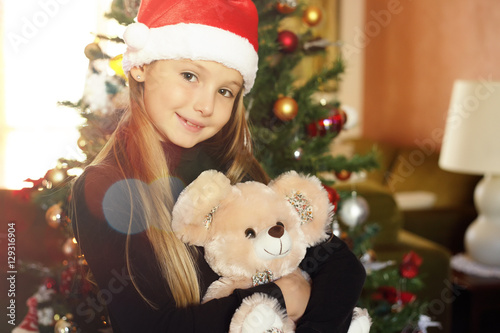 Bambina col cappellino di Natale abbraccia il suo orsacchiotto photo