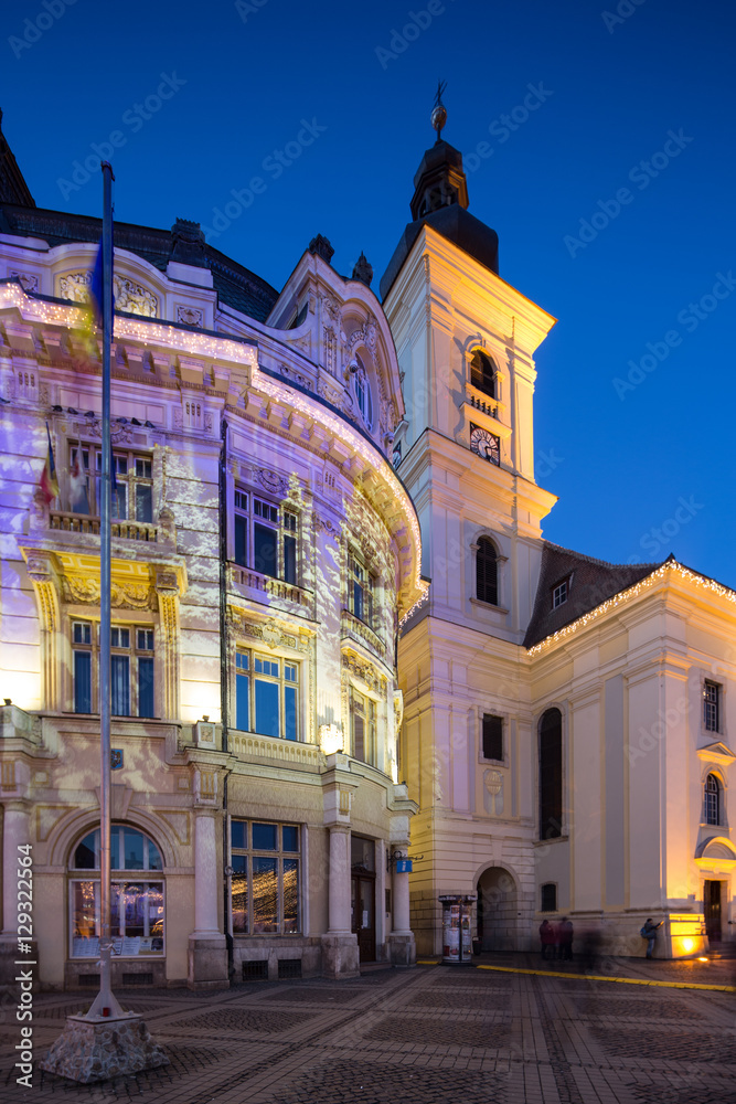 Twilight image of the City Hall and Holy Trinity Roman-Catholic church in Sibiu with architectural lights projecting Christmas images on the walls.