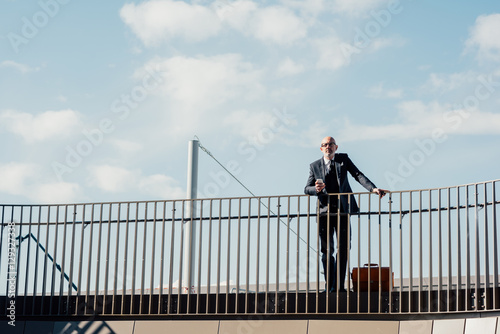 Middle-age contemporary businessman leaning on a handrail holding smart phone - work, business, technology concept