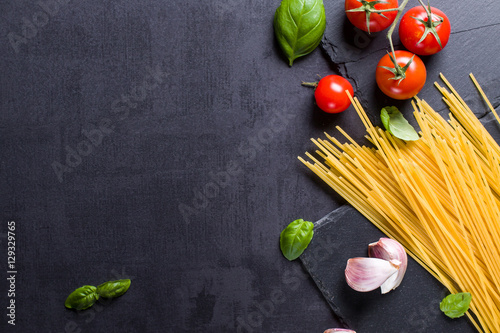 Food ingredients for Italian spaghetti on black stone slate background with much copy space of your project.