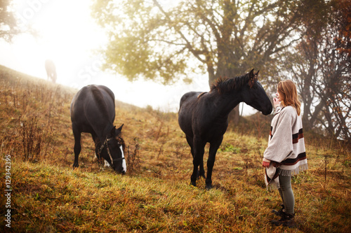 Woman with her horses. Concept about people and animals. Early morning. Misty mountain. Woman in boho style.