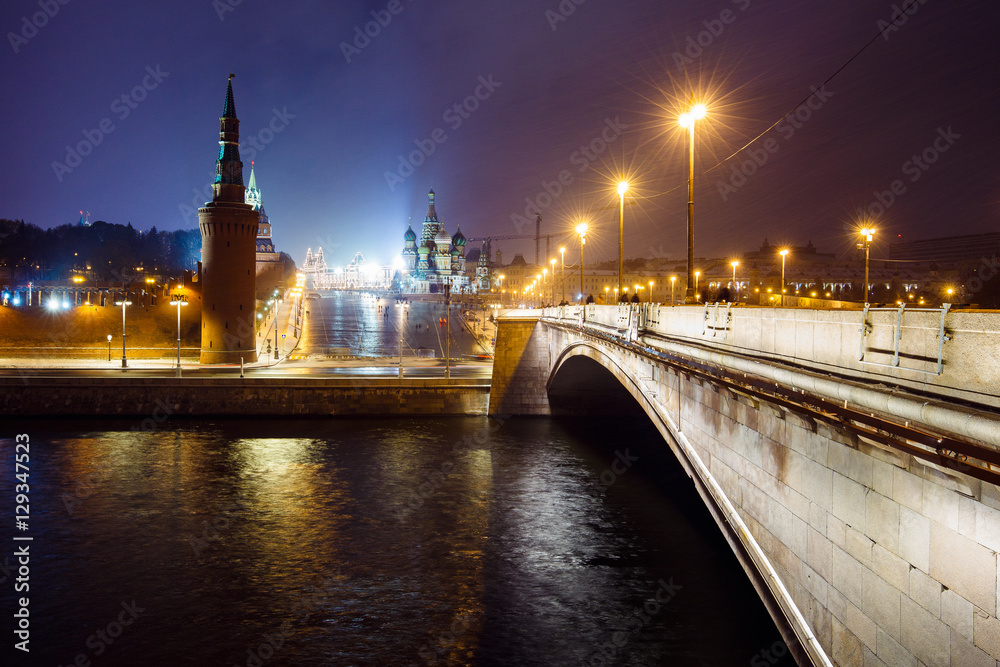 Fototapeta premium Night cityscape view of Moscow Kremlin, Basil's Descent and Red Square, embankment, strret light at evening winter snowfall from Bolshoy Moskvoretsky Bridge in Moscow, Russia. Long exposure.