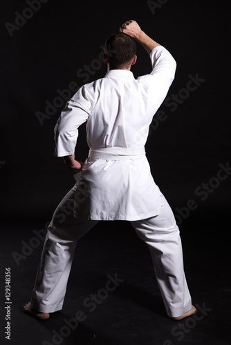 Karate man in a kimono in fighting stance on black background