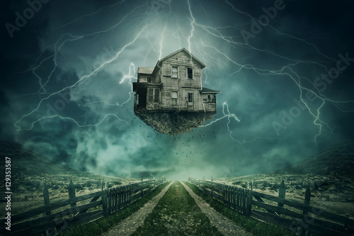 Rapture surreal concept. Ghost house ripped from the ground flying above a country road in a stormy day with lightnings in the sky. photo