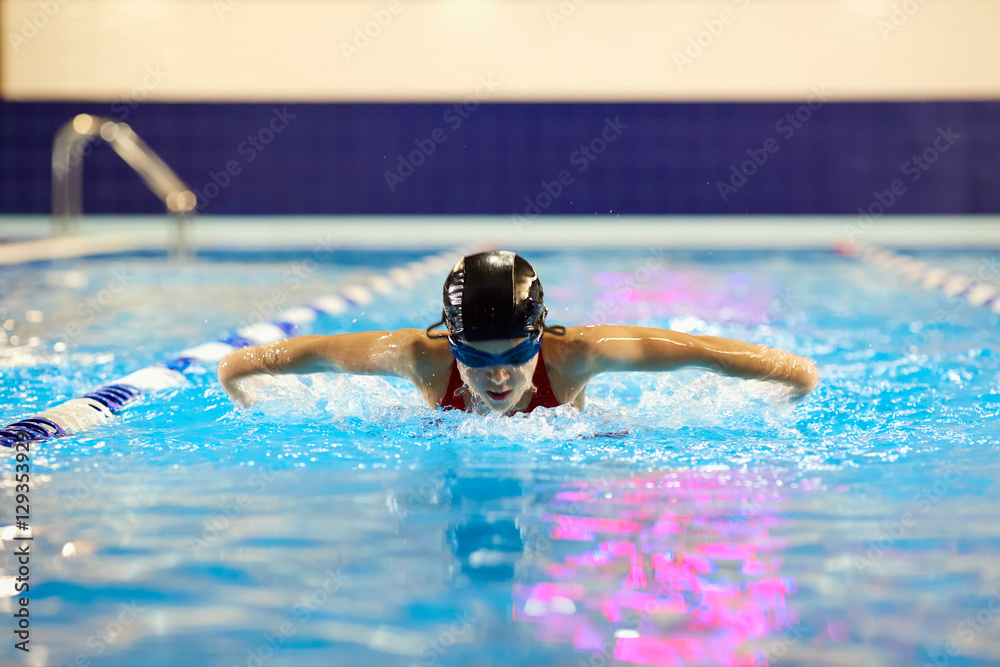 Swimmer girl teenager in the pool swims butterfly inside