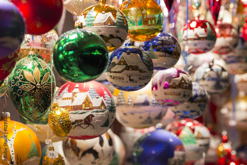 Schöne, handbemalte, bunte Christbaumkugeln und Weihnachtsdekorationen hängen eng beieinander an einem Verkaufsstand eines Weihnachtsmarkts und warten auf potenzielle Käuferinnen und Käufer