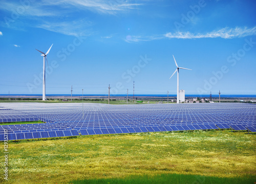 Modern solar station with blue panels and windfarm with wind tur