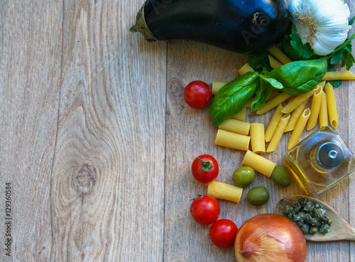  raw Ingredients for italian dish : pasta, vegetables , olive oil and aromatic herbs on wooden table with space