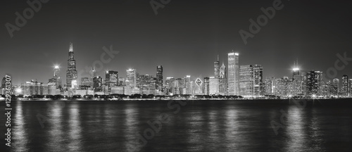 Black and white panoramic picture of Chicago city skyline with reflection in Lake Michigan at night.