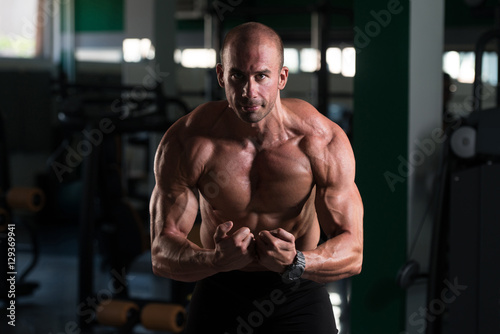 Fototapeta Naklejka Na Ścianę i Meble -  Muscular Man Flexing Muscles In Gym
