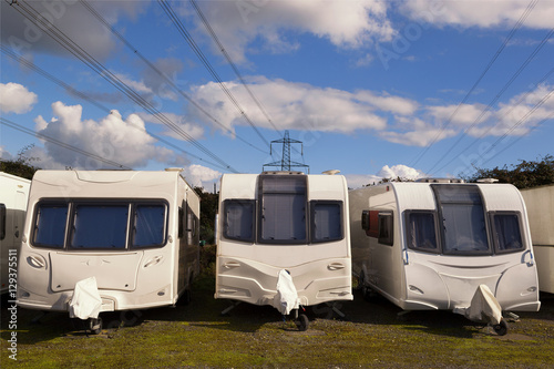 Three Caravans stored in rows on a sunny day with clouds in the sky with electricity cables in the background. Space for text.