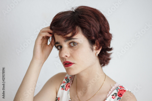 Portrait of a girl with short hair and a flower dress on a white background. She has brown eyes.