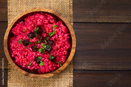 Beetroot risotto prepared with beetroot puree, roasted beetroot pieces and parsley on the top, photographed overhead on dark wood with natural light (Selective Focus, Focus on the top of the risotto)