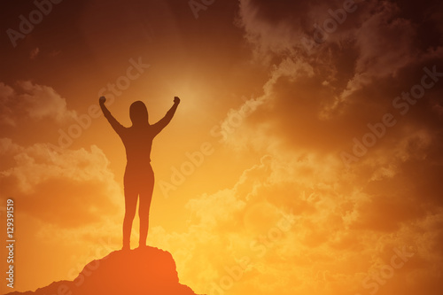silhouette of winning success woman at sunset or sunrise standing and raising up her hand in celebration of having reached mountain top summit goal.Happy celebrating.business success concept