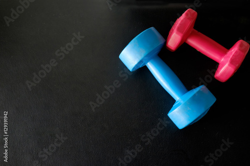 Blue and pink dumbbells on dark leather background.