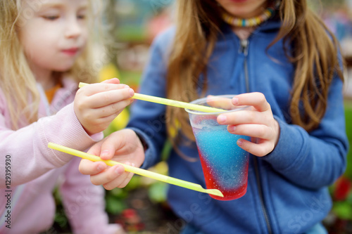 Tableau sur toile Two cute little sisters drinking frozen slushie drink